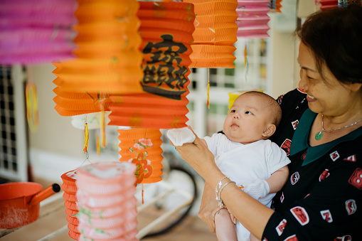 Image of an Asian Chinese senior carrying her grandson and celebrating traditional Chinese lantern festival at home