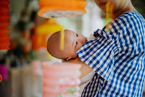 Image of an Asian Chinese woman carrying her baby and celebrating traditional mid autumn festival at home