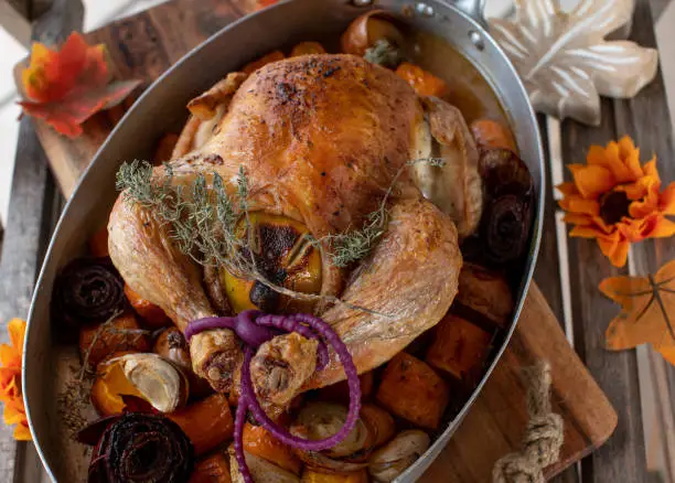 Homemade whole roasted chicken with root vegetables. Served in a rustic roasting pan on wooden background. Delicious poultry dish for autumn and thanksgiving season.