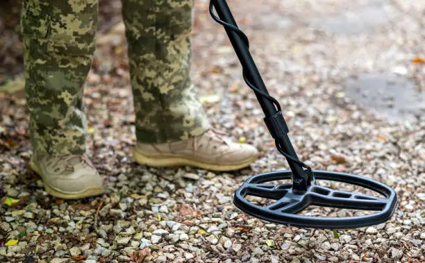 Military sapper with a metal detector in the field. Ukrainian Explosive Ordnance Disposal Officer detecting metal by metal detector device