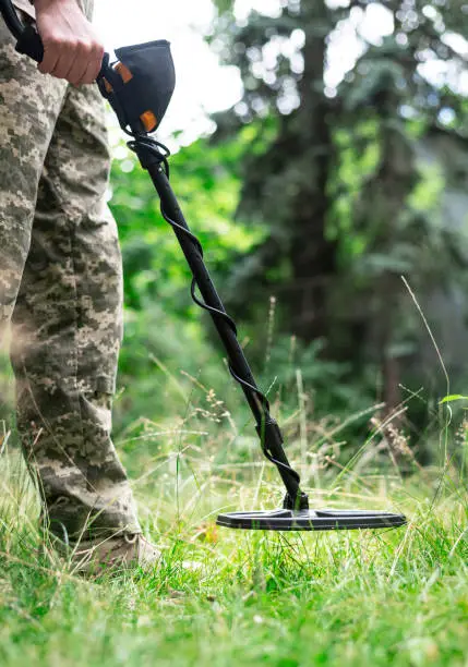 Soldier using a metal detector in fields. Ukrainian Explosive Ordnance Disposal Officer detecting metal by metal detector device