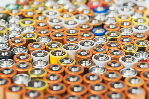 Close up of positive ends of colorful discharged batteries of different sizes and formats, top view, selective focus. Used alkaline battery Hazardous garbage concept.