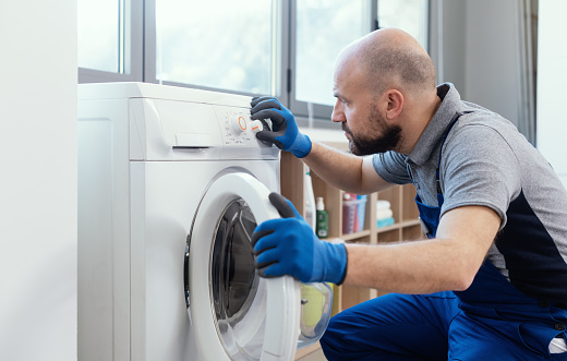 Professional technician checking a washing machine, he is adjusting a knob, home repair concept