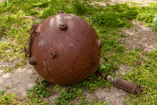 A rusty naval mine lies on the ground in green grass