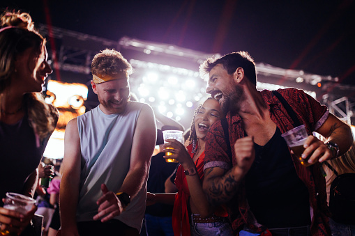 Cheerful group of friends, standing in crowd at music festival, drinking alcohol, dancing and having a good time
