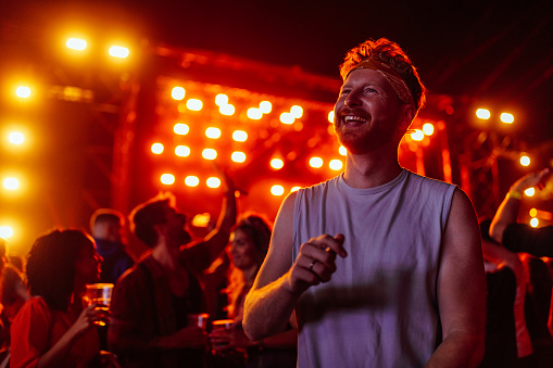 Smiling ginger man dancing in crowd at music festival and having a good time