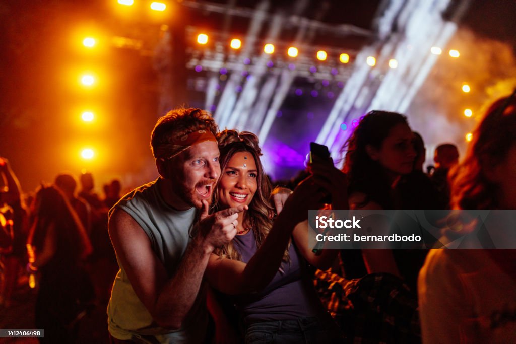 Young couple in a crowd at a concert Two beautiful friends taking selfie with a samrtphone on a music festival Music Festival Stock Photo