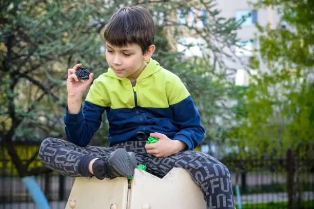 Photo of Boy playing with modern spin top outdoors. Entertainment game for children. Top, triggered by a trigger. Kid demonstrate two different variants choosing which is better