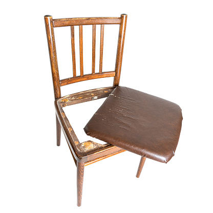 Old and broken dining chair with a shabby cracked seat isolated on white background