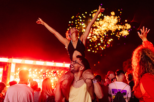 Young happy couple dancing under the fireworks on the sky by night. Man is carrying his girlfriend on shoulders