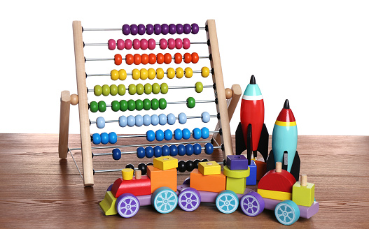 Bright toy train, abacus and rockets on wooden table against white background