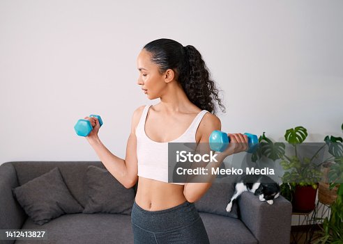 istock A serious young woman lifts small weights to get strong at home 1412413827