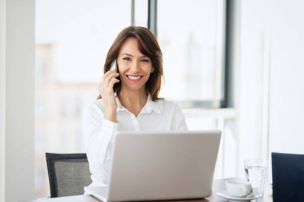 istock Businesswoman using mobile phone and laptop while working at office desk 1412414777