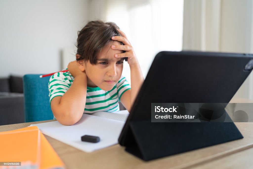 Child sitting alone at home and feeling stressed while doing her homework Child Stock Photo