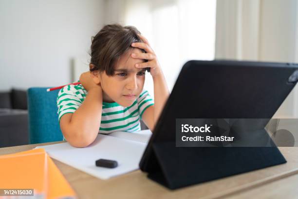 Child Sitting Alone At Home And Feeling Stressed While Doing Her Homework Stock Photo - Download Image Now