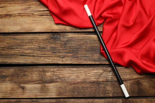 Beautiful black magic wand and red fabric on wooden table, top view. Space for text