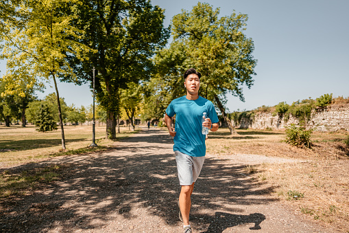 A handsome young Chinese athlete man running outdoors in a park.