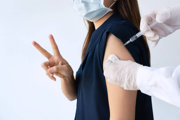 gros plan du médecin dans des gants médicaux tenant une seringue et nettoyant la peau sur le haut du bras avant l’injection antivirale. femme asiatique se faisant vacciner contre le covid-19 en clinique ou à l’hôpital sur fond blanc. - cold and flu vaccination injecting aids photos et images de collection