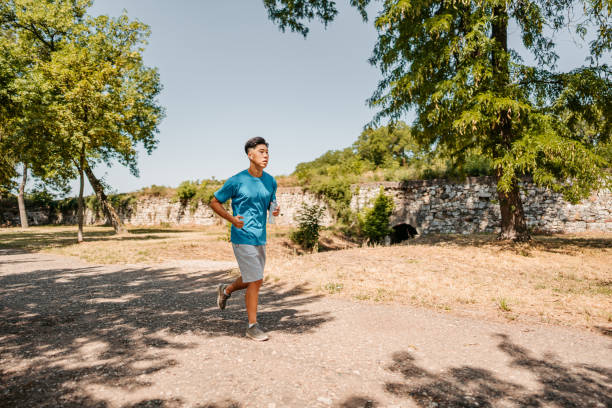 A handsome young Chinese athlete man running outdoors in a park.
