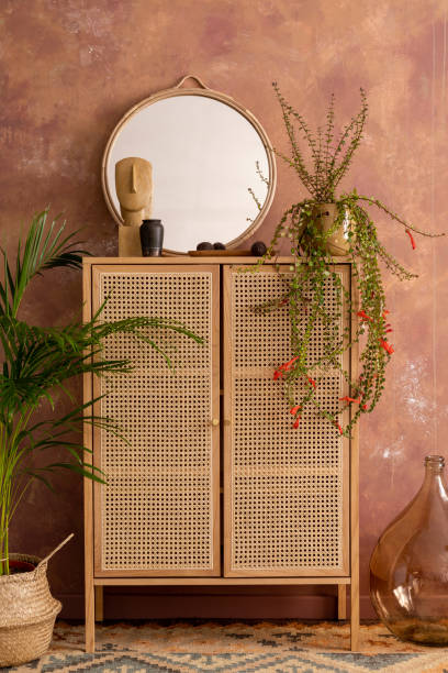 istock Stylish boho vintage dining room interior with rattan commode, round mirror, plants and personal accessories. Brown wall. Template. 1412418706