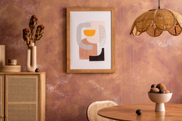 istock Creative interior design of dining room interior with poster mock up. Round table with rattan chair, commode and flowers. Brown wall and rattan lamp. Mock up poster. Template. 1412418784