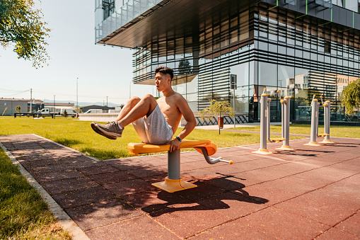 A handsome young Chinese man doing sit-ups outdoors in a public park.