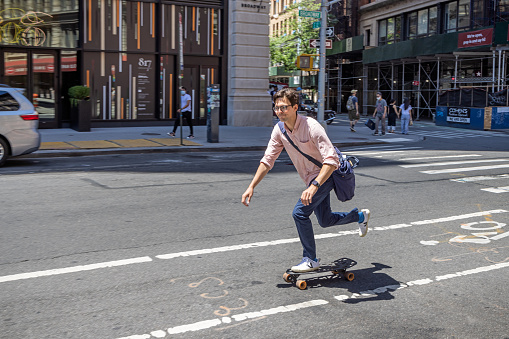 Young man with glasses driving down Broadway on a skateboard in Lower Manhattan