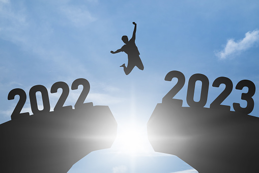 Concept Happy new year 2023 Silhouette image of happy man jump from 2022 up to 2023 on blue sky background.