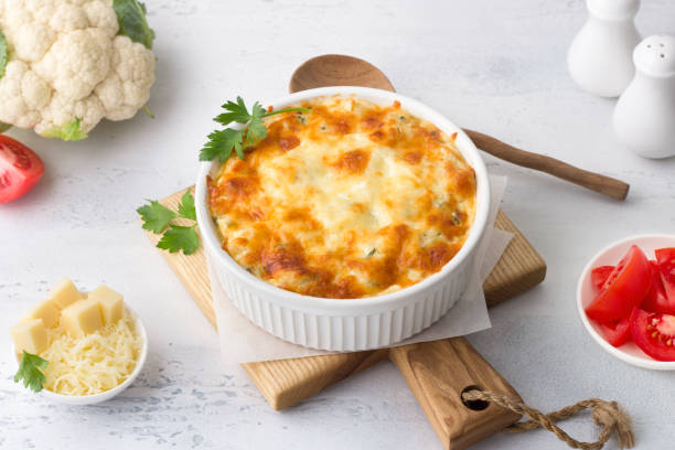istock Homemade cauliflower casserole with tomatoes and cheese on a light gray background with ingredients. Delicious vegetarian food 1412421087