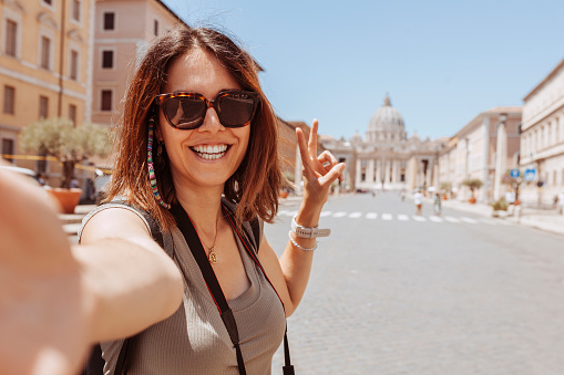 Europe luxury travel vacation tourist in Rome, Italy. Vacation cheerful woman taking selfie photo with phone doing v sign with fingers at Vatican city St Peter's Basilica church. Summer holiday destination.