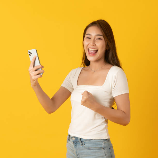 istock Surprise happy asian beautiful woman isolate on yellow background using smartphone 1412422310