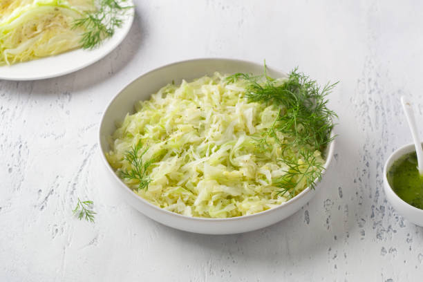 istock Steam white cabbage in a white ceramic bowl with herbs and green sauce on a light blue background, top view. Delicious diet food 1412422367
