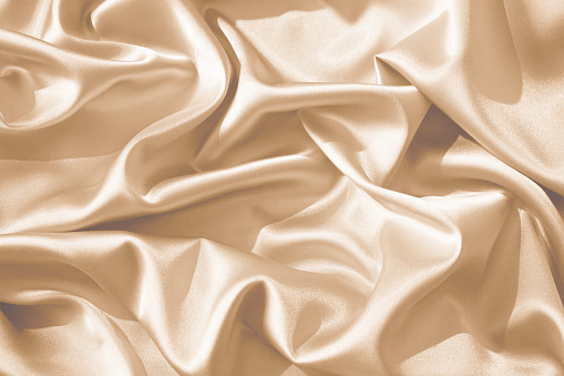 Cream beige silk satin. Wavy folds pattern. Silky soft fabric. Pale yellow color. Elegant background with space for design. Luxurious. Wedding, valentine, romance.