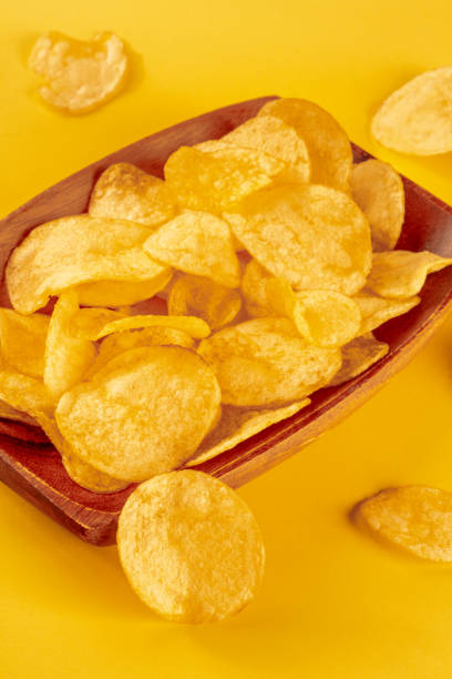 istock Potato chips or crisps in a bowl and scattered on a yellow background 1412423305