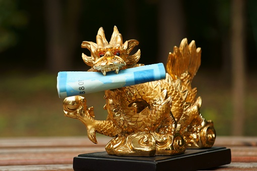 A figurine of a Chinese dragon with money in its teeth in close-up. The symbol of Feng shui. A symbol of power and a mighty will. A wise and reliable patron.