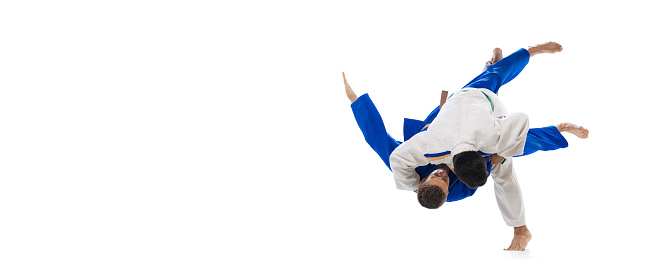 Studio shot of two men, professional judo athletes training isolated over white background. Sweeping hip throw. Concept of martial art, combat sport, health, strength, energy. Copy space for ad, flyer