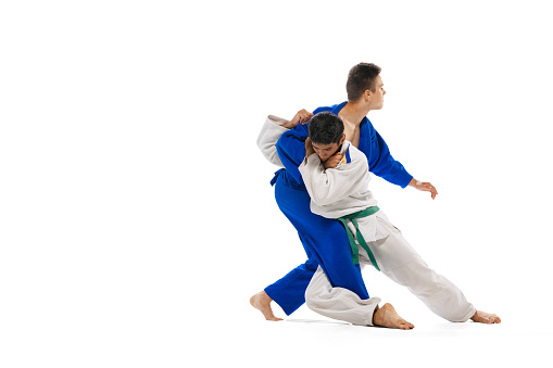 Studio shot of two men, professional judo athletes training isolated over white background. Sweeping hip throw. Concept of martial art, combat sport, health, strength, energy, fit. Copy space for ad