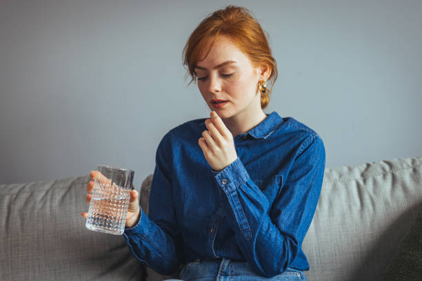 jeune belle femme prenant un comprimé avec un verre d’eau fraîche. c - painkiller photos et images de collection