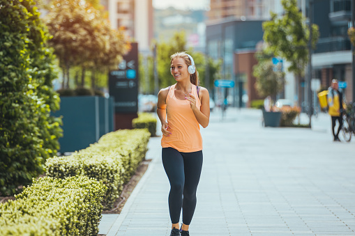 Young female runner in a sports bra is jogging in the city street. full length of Urban female runner training on summer. Sporty woman running and exercising