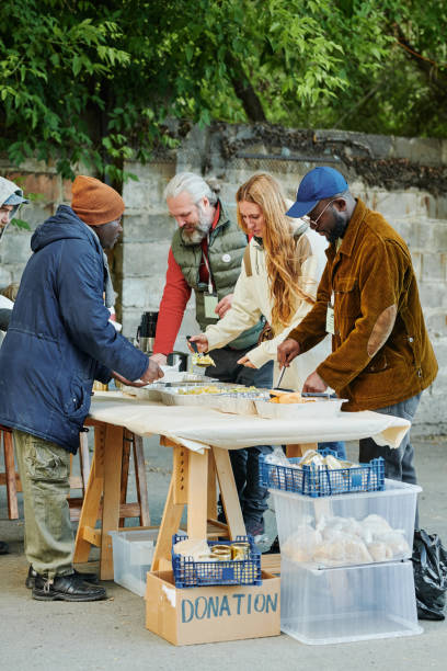 Volunteers feeding homeless people with food Group of volunteers serving homeless people giving them food while standing outdoors doing a favor stock pictures, royalty-free photos & images