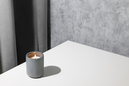 Candle soy homemade in ceramic burning in grey modern interior room, atmosphere and minimalistic composition side view with copy space