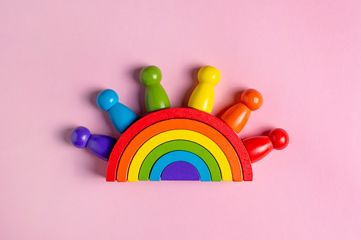 Colorful Waldorf wooden human figure rainbow in a montessori teaching pedagogy on pink background, kid play concept top view