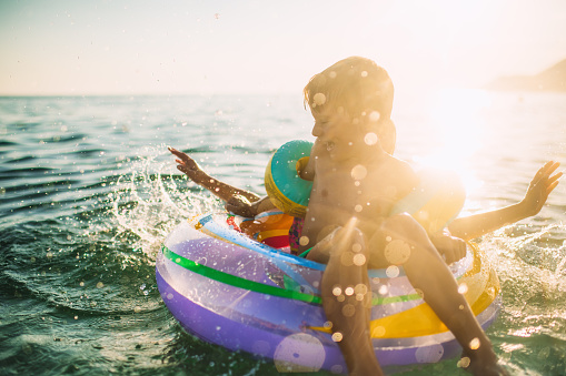 Little boy and girl swimming, splashing and playing in the sea with inflatable ring