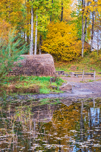 Grass hut at a forest lake with autumn colors