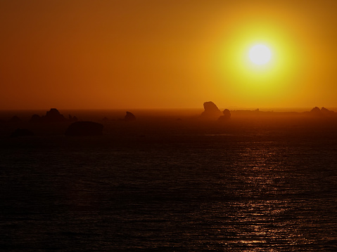Orange ocean sunset over distant sea stacks.
