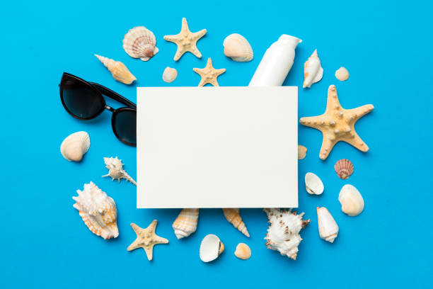 istock Summer time concept with blank greeting card and blank white paper on colored background. Seashells from ocean shore in the shape of frame separated with space for text top view 1412439752