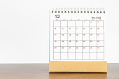 The December 2022 desk calendar with plant on wooden table.