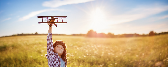 Boy plaing with retro wooden plane on the field in sunset. Concept of the family vacation, dreaming and future aspiration.