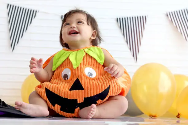 Adorable baby girl kid dressing up in orange fancy Halloween pumpkin costume, cheerful little cute child go to party, playing trick or treat, Happy Halloween celebration.