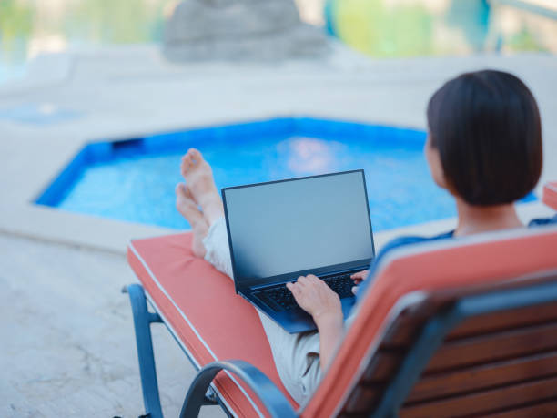 istock Young business woman working at computer by hotel pool. 1412450048
